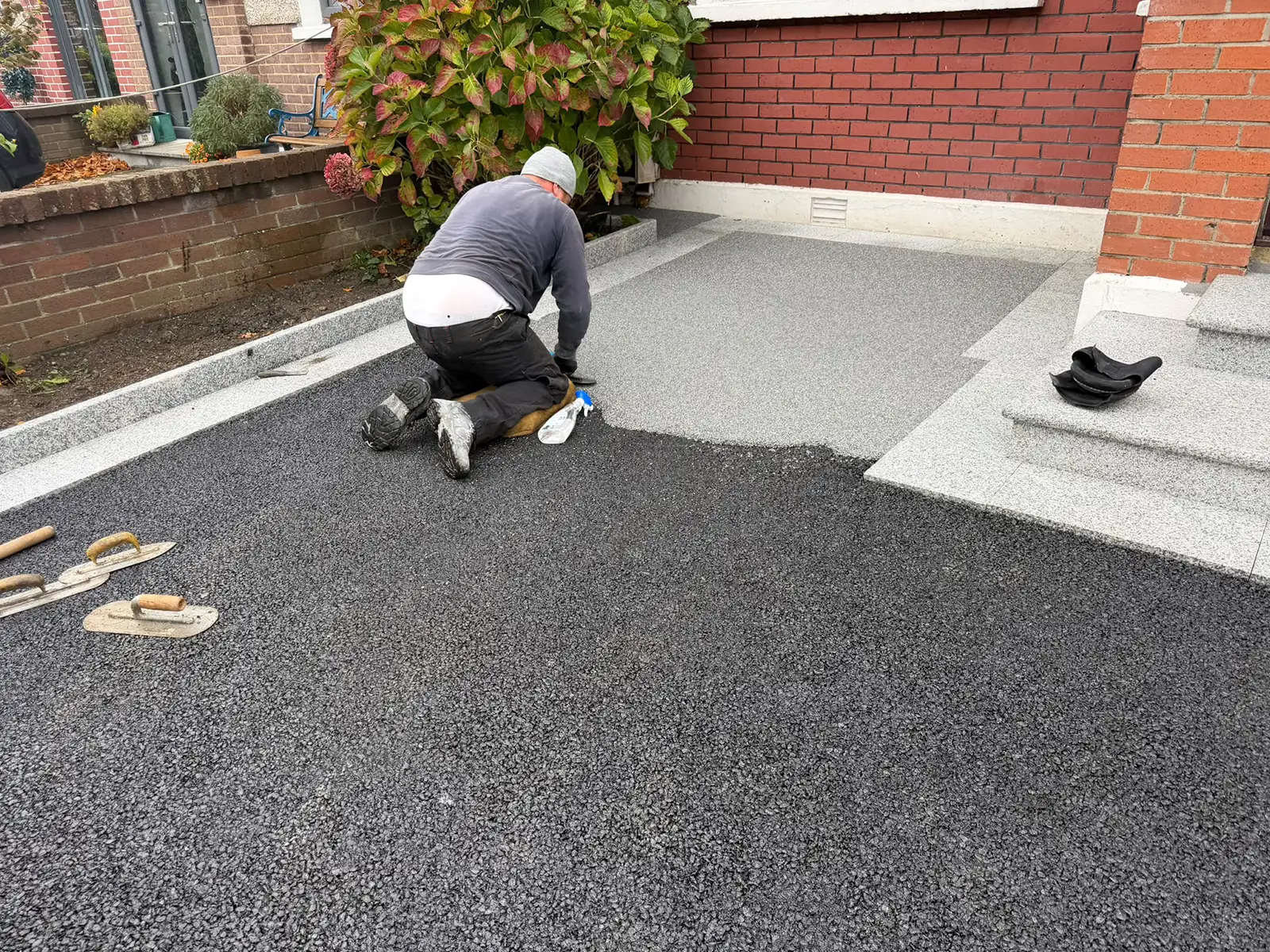 Resin-bound aggregate being trowelled over the prepared tarmac base beside granite steps on Kilnamanagh Road